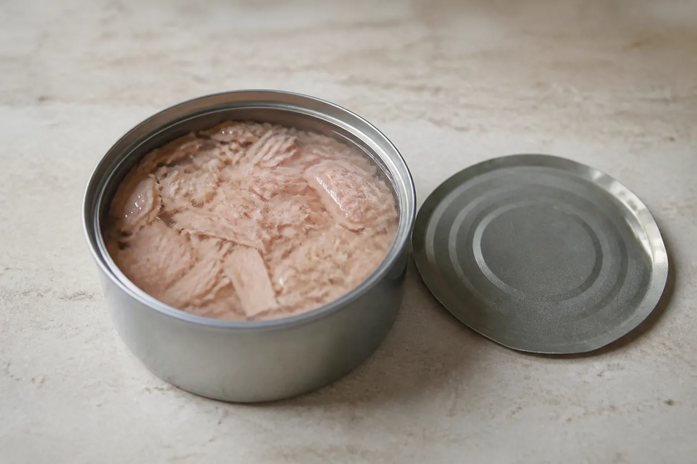 An open tin of tuna in spring water beside its lid on a kitchen counter
