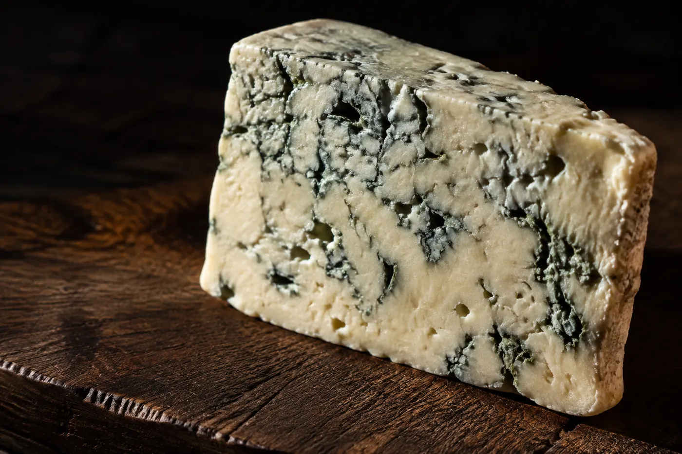 A wedge of blue veined cheese on a dark board