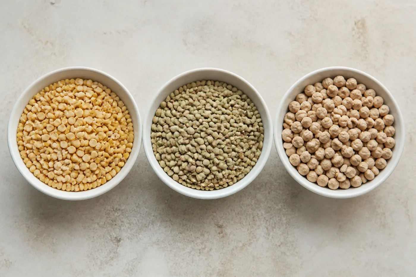 Dried peas, lentils, and chickpeas in small dishes on a worktop