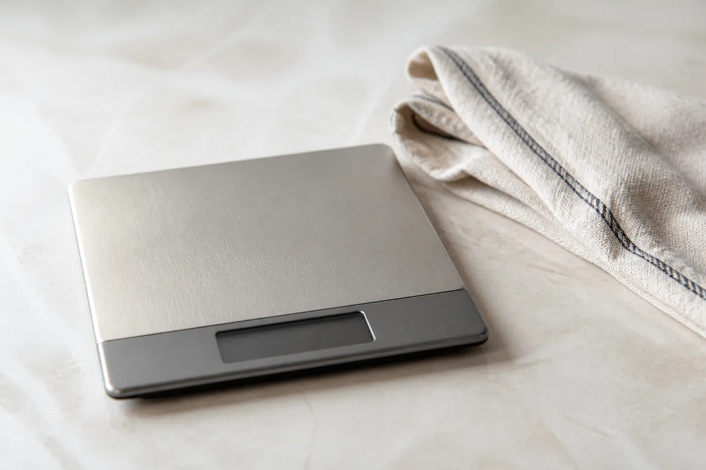 A set of digital kitchen scales on a worktop beside a folded towel