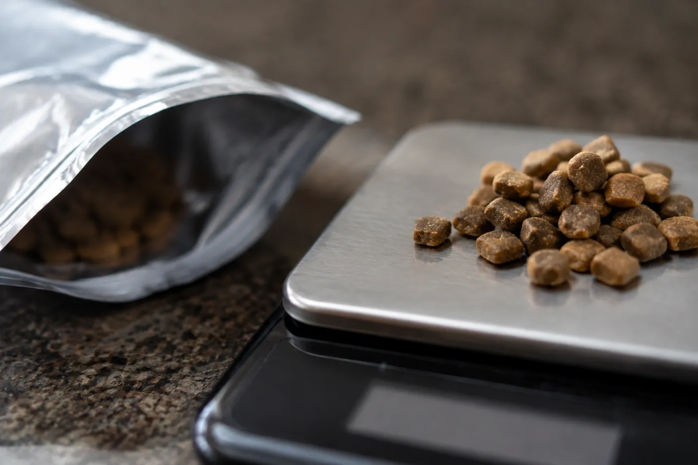 An opened food pouch and a measured heap of kibble on a digital scale