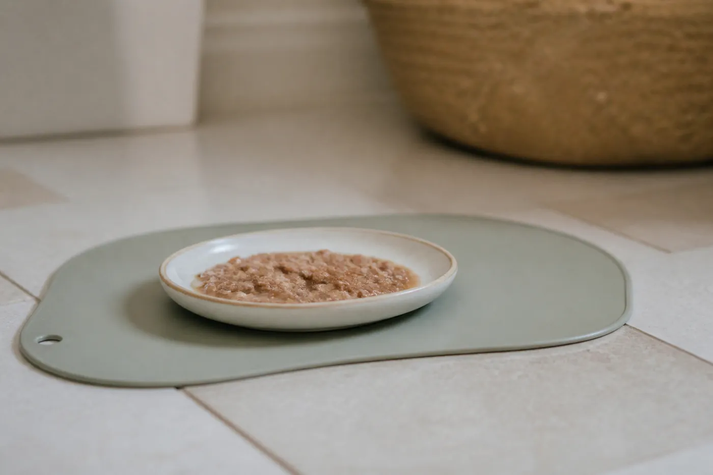 A shallow dish of wet kitten food on a low feeding mat on a tiled floor