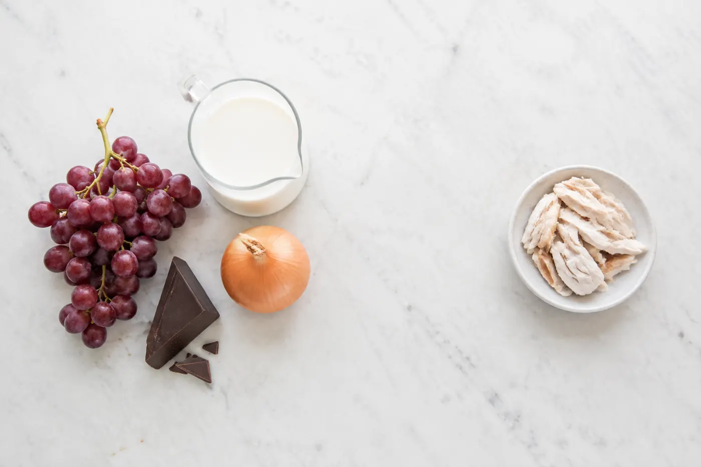 A kitchen worktop from above with dark chocolate, walnuts, almonds, oats, blueberries, strawberries, banana and mixed seeds arranged in separate groups