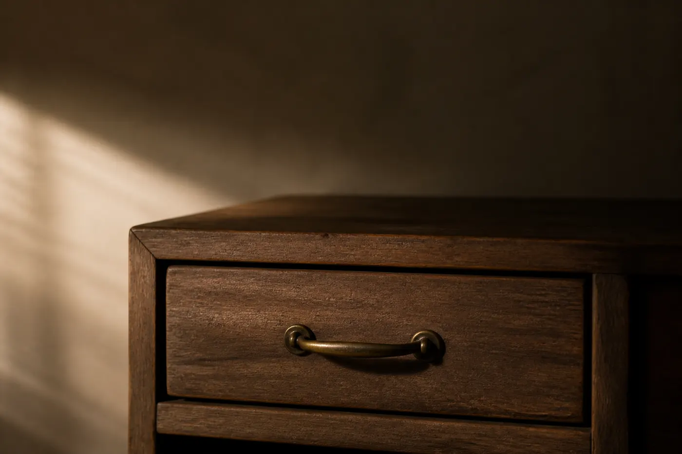 A small closed wooden drawer with a brass handle in soft side light