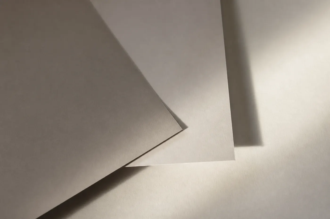 Two plain sheets of paper overlapping at right angles in raking light